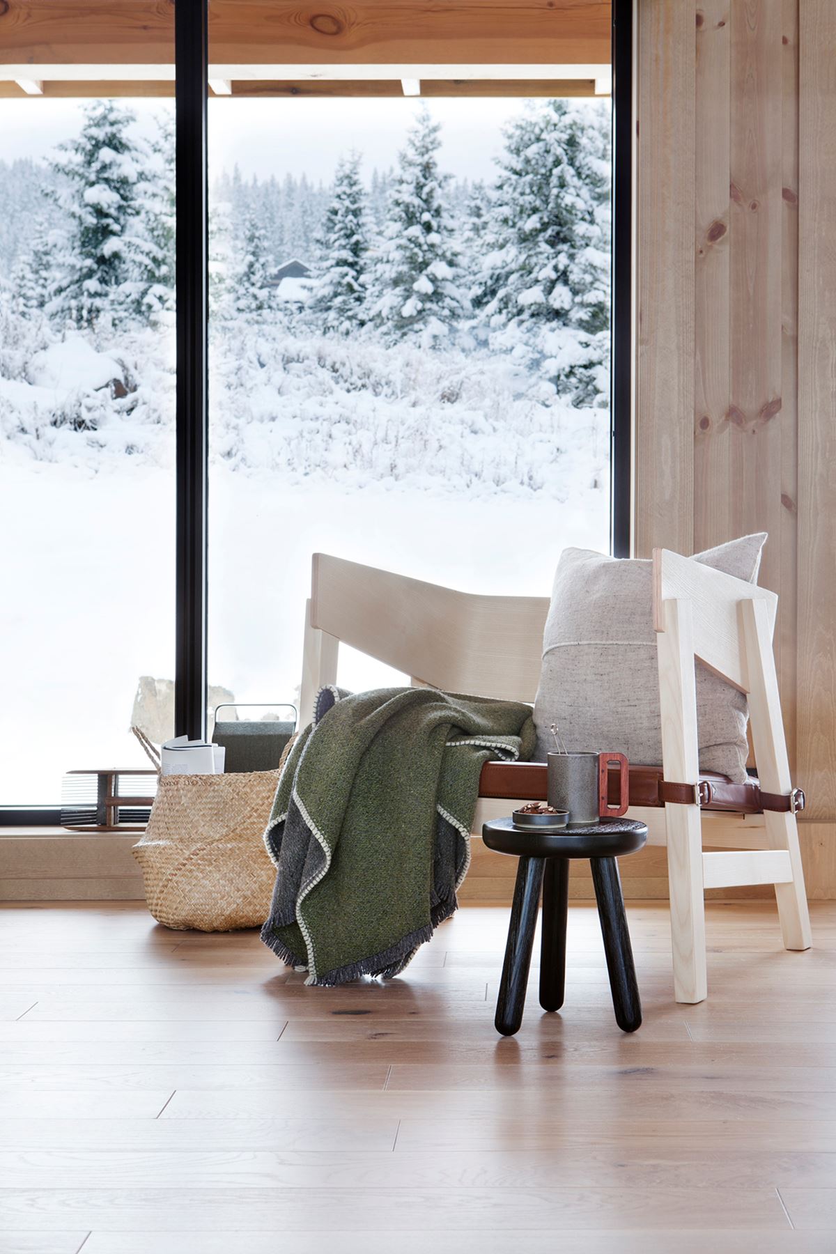En moderne stol med et grønt pledd. I bakgrunn er det et stort vindu som viser det snødekte landskapet