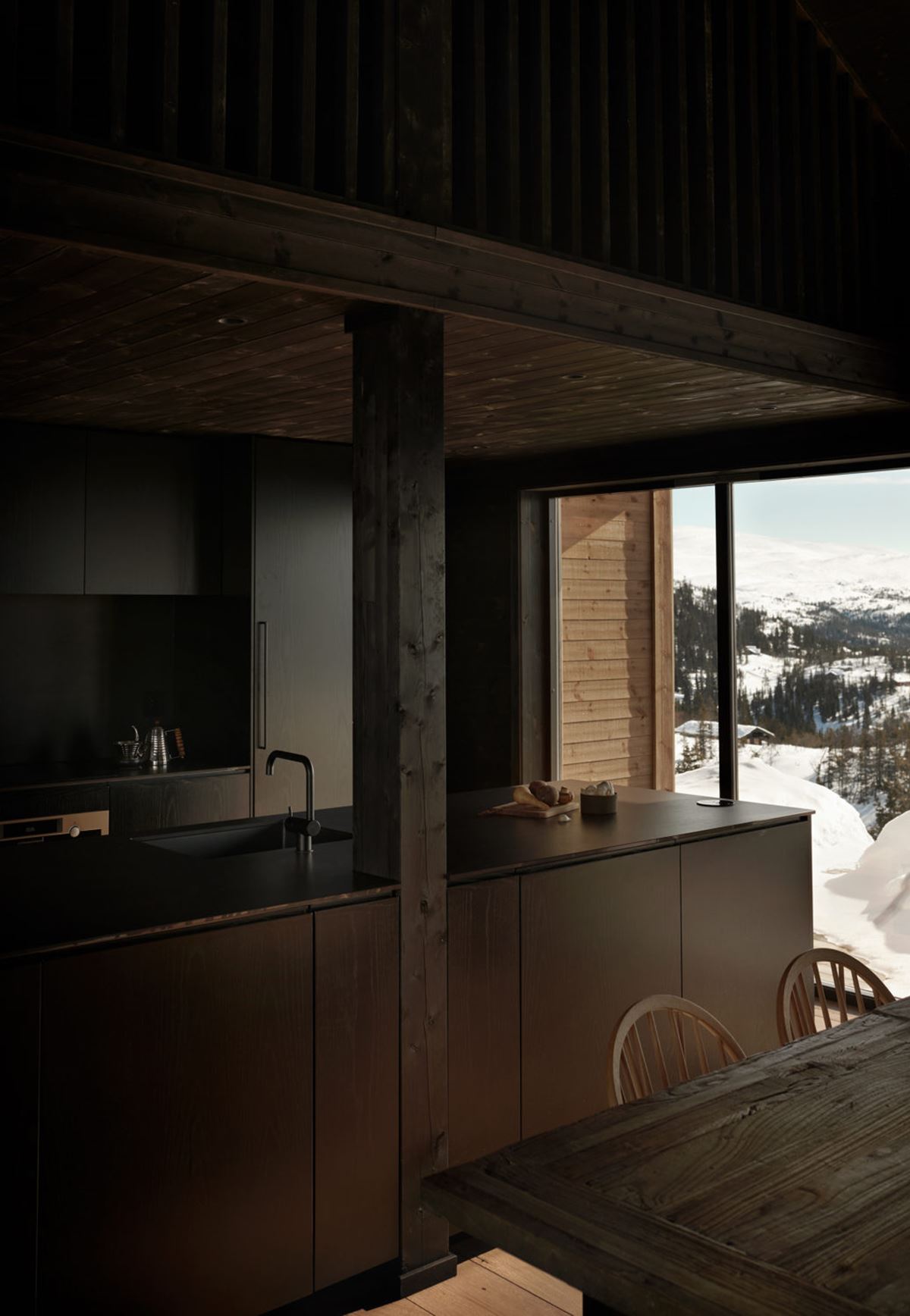 Et mørk kjøkken blir lyst opp av store vinduer og en utsikt over snødekte landskap
