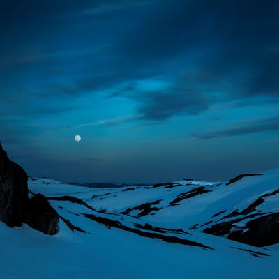 Fullmånen lyser over mørke, snødekte fjelltopper