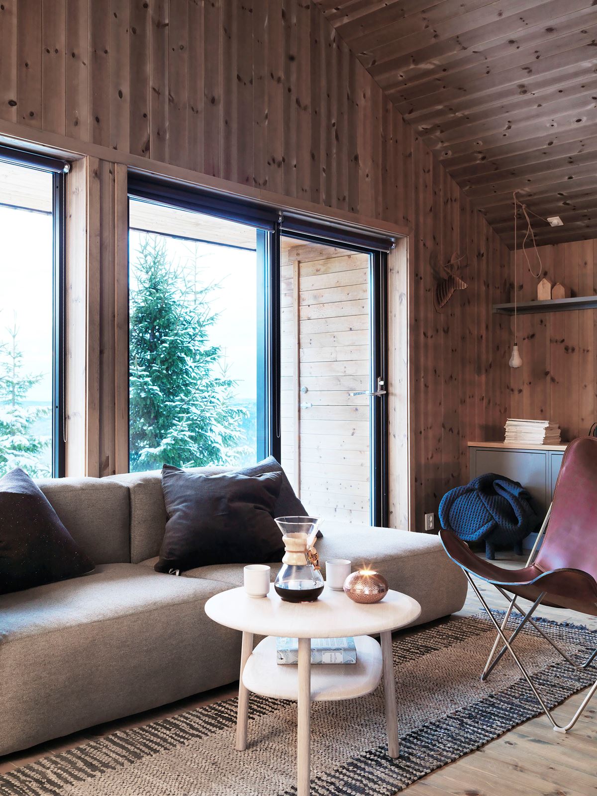 En grå sofa på hytta. I forkant står et bord med kaffekanne og kaffekopper