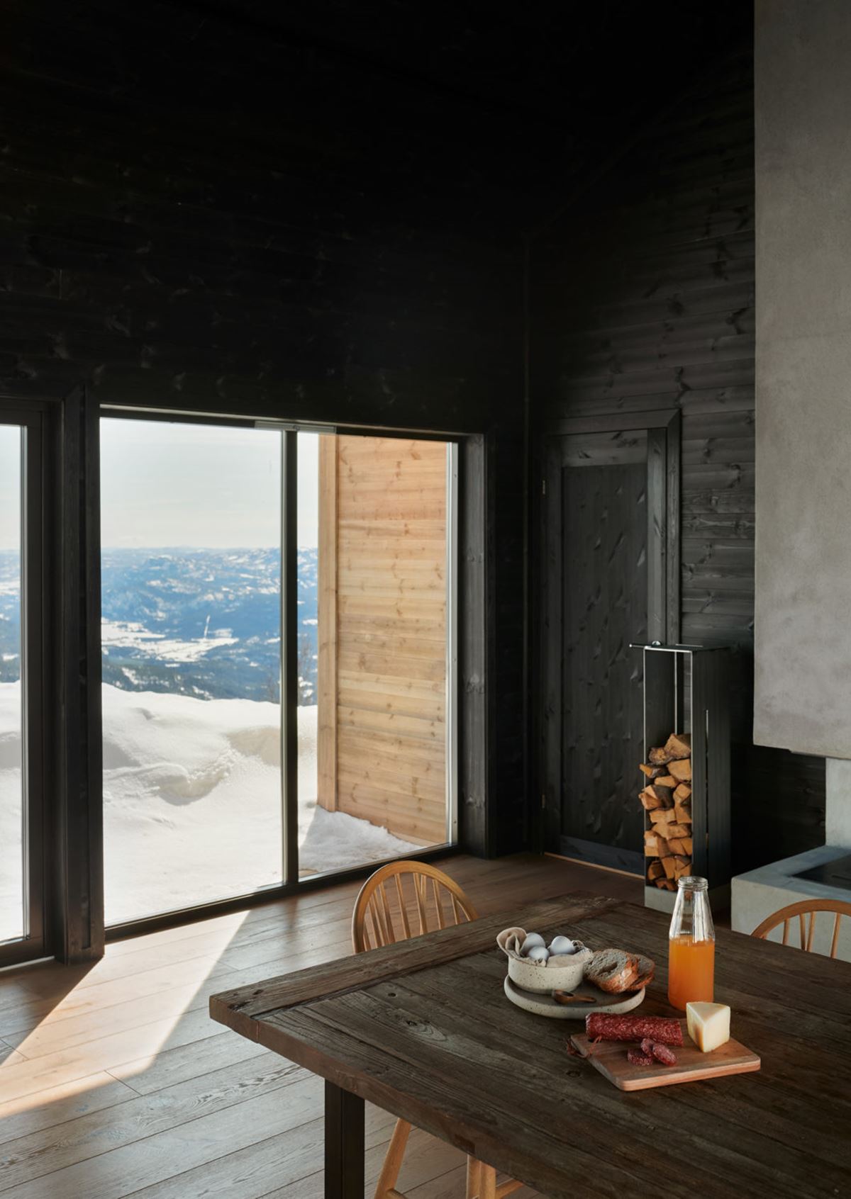 På et mørkt trebord står juice og frokostvarer. I bakgrunnen skimtes en utsikt over daler, fjell og snødekt natur.