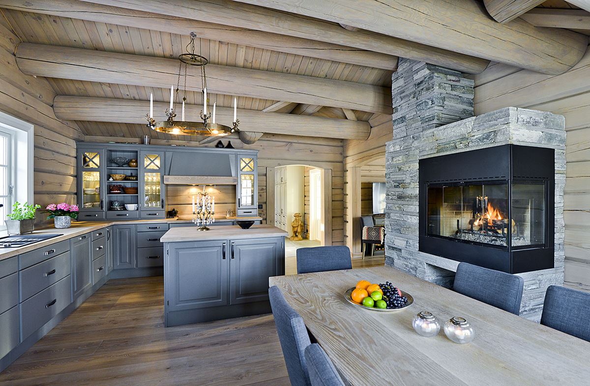Et kjøkken i grått treverk i en laftet hytte. Til høyre står en stor peis i skifer