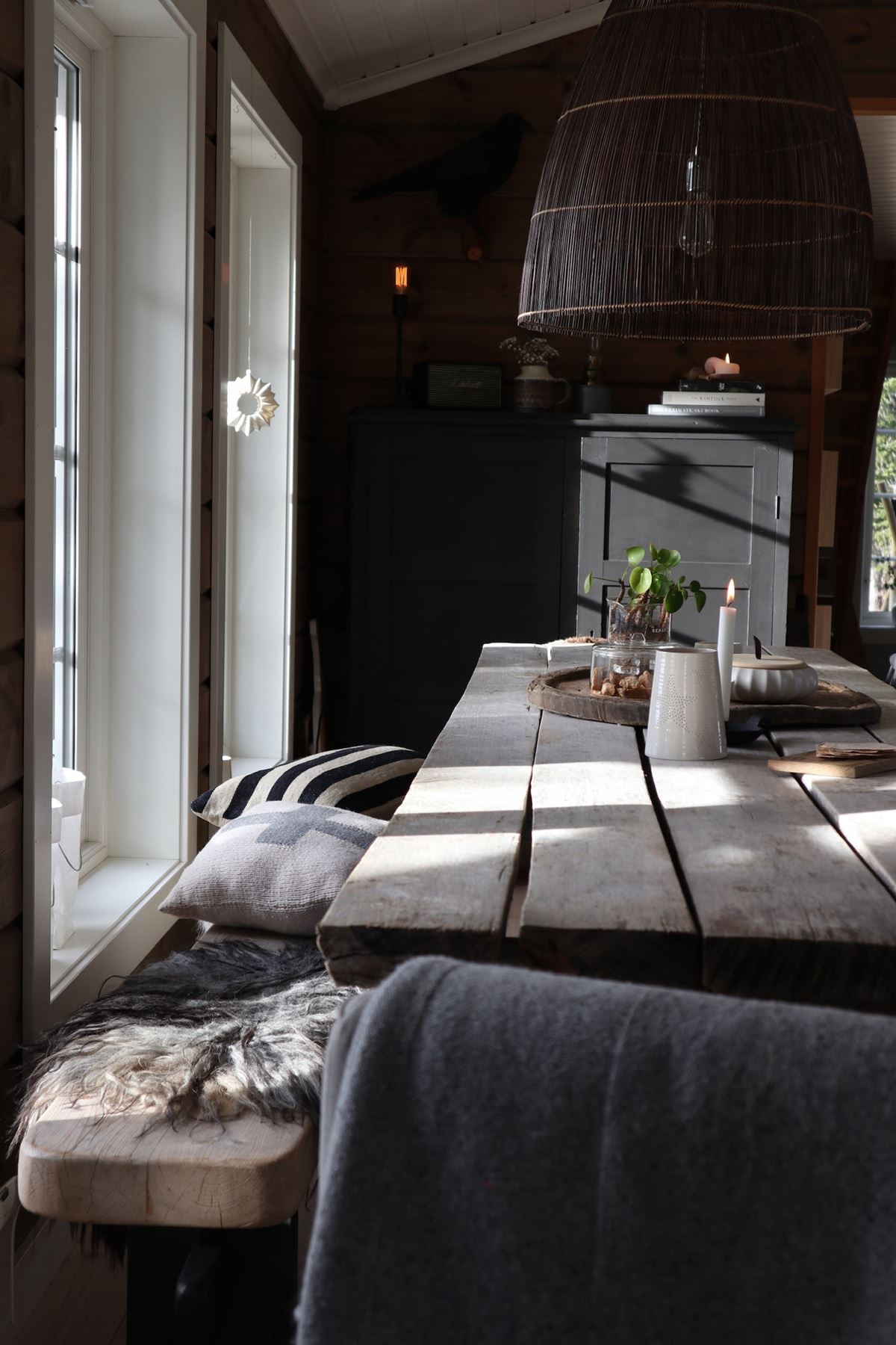 Et mørkt, rustikt spisestuebord. Til venstre står en benk med ulike tekstiler. 