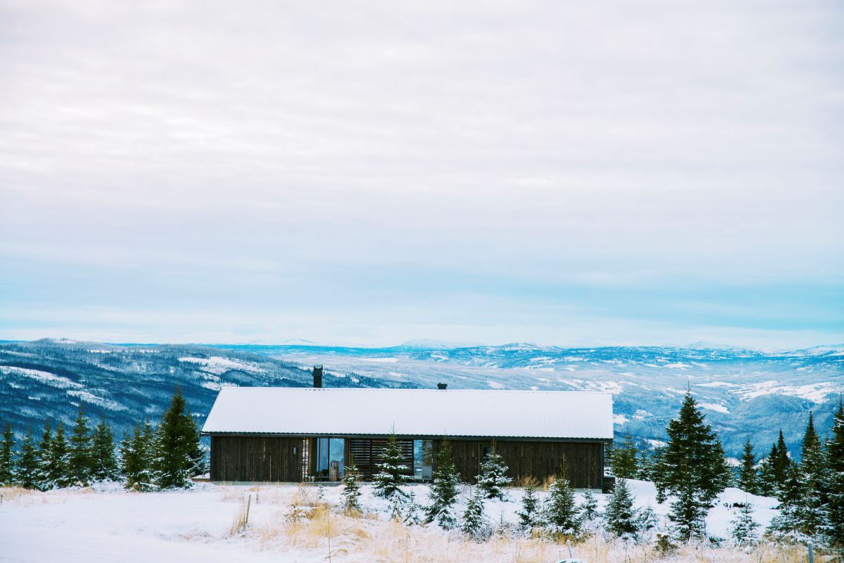 En mørk hytte ligger i et snødekt fjellandskap